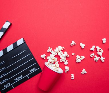 Cinema film concept. Fresh salty pop corn and movie clapper board, red color background, top view